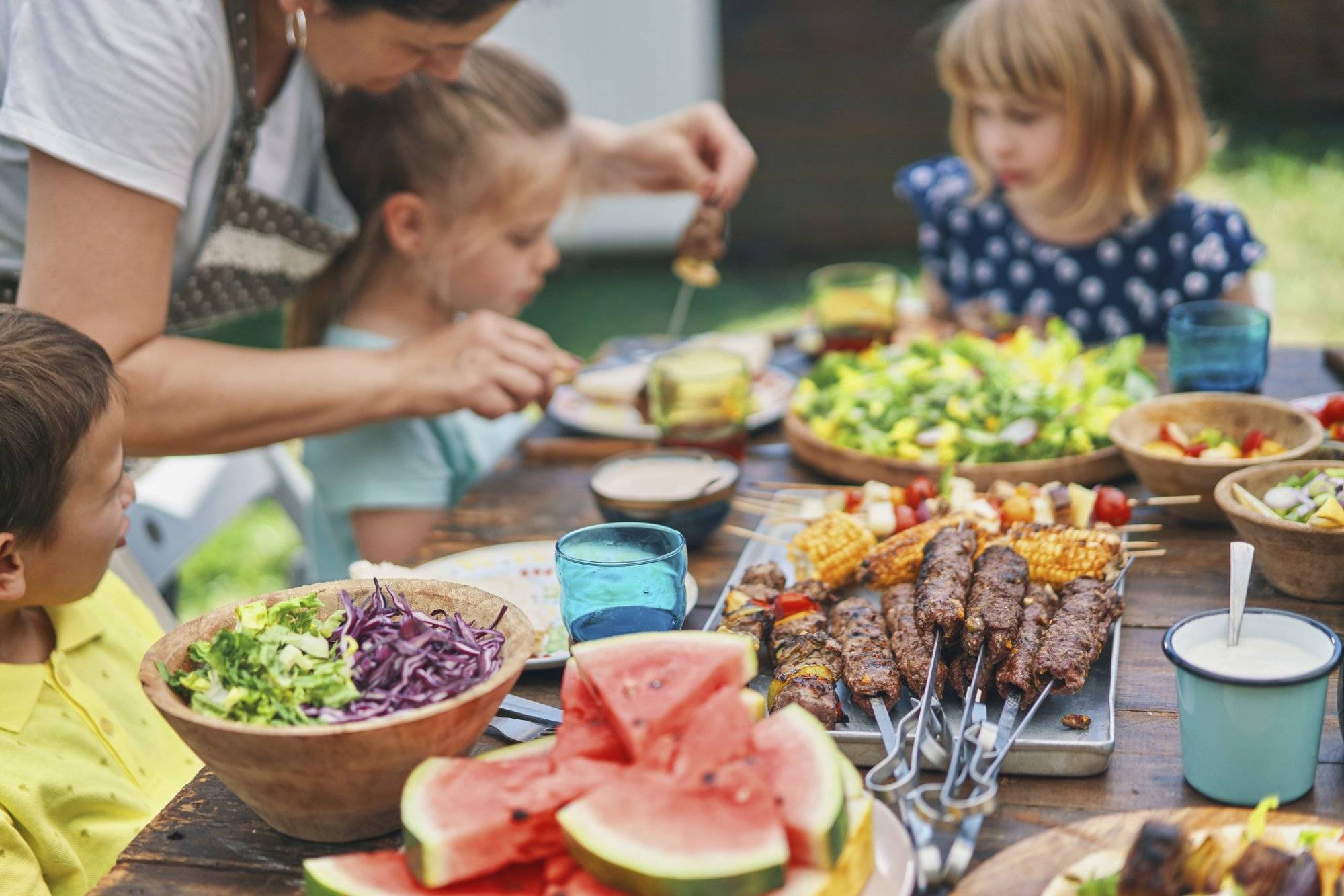 Young Family Eating Lamb, Beef and Vegetable Kebab with Green Salad Outside Young Family Eating Lamb, Beef and Vegetable Kebab with Green Salad Outside