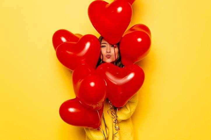 Woman’s face hiding between red balloons on yellow background. Woman's face hiding between red balloons on yellow background.